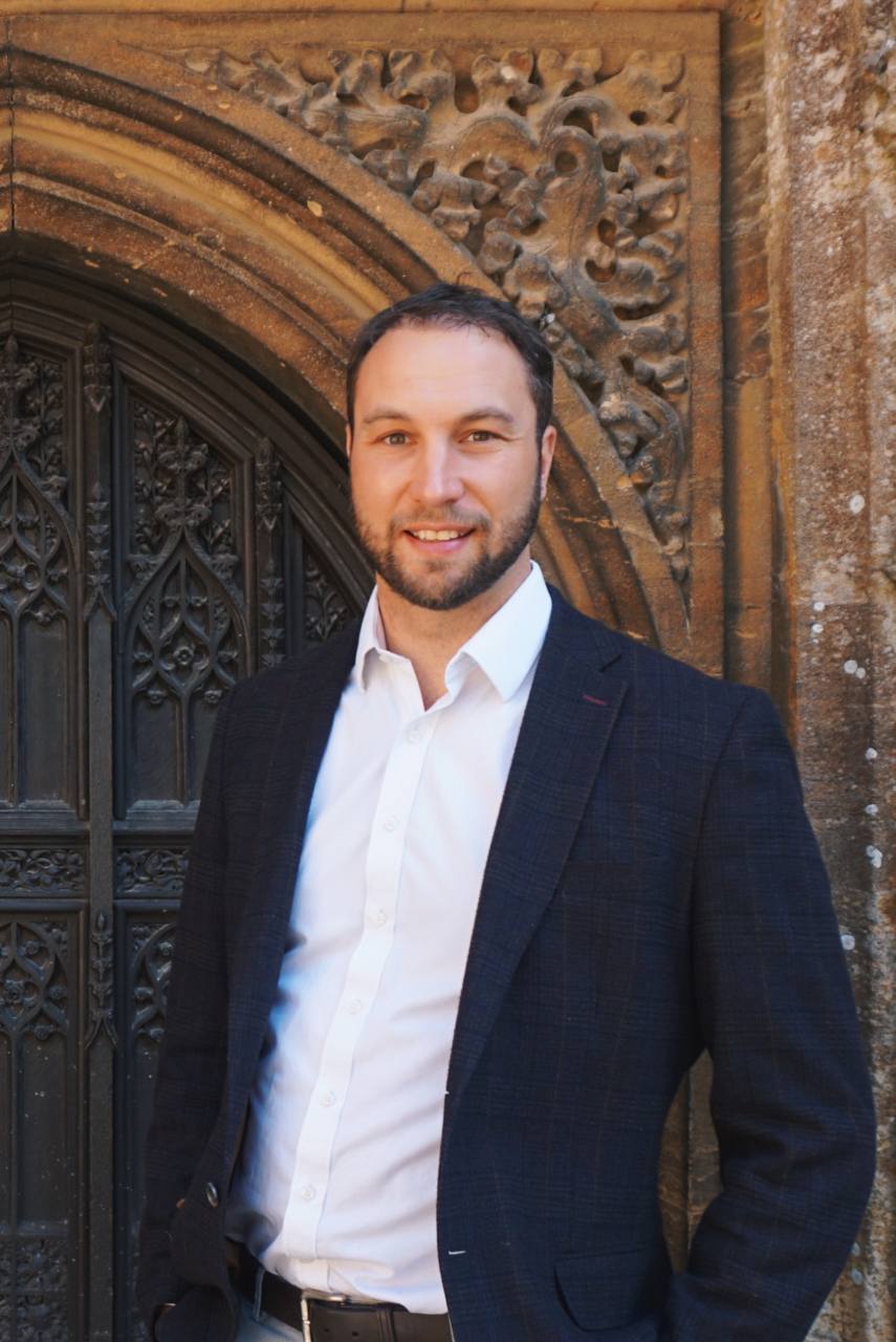 Lloyd, smiling, standing in front of a carved stone archway